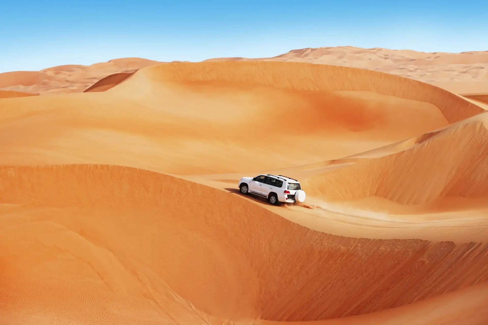 Desert Safari A 4x4 vehicle navigates through golden sand dunes against a clear blue sky.
