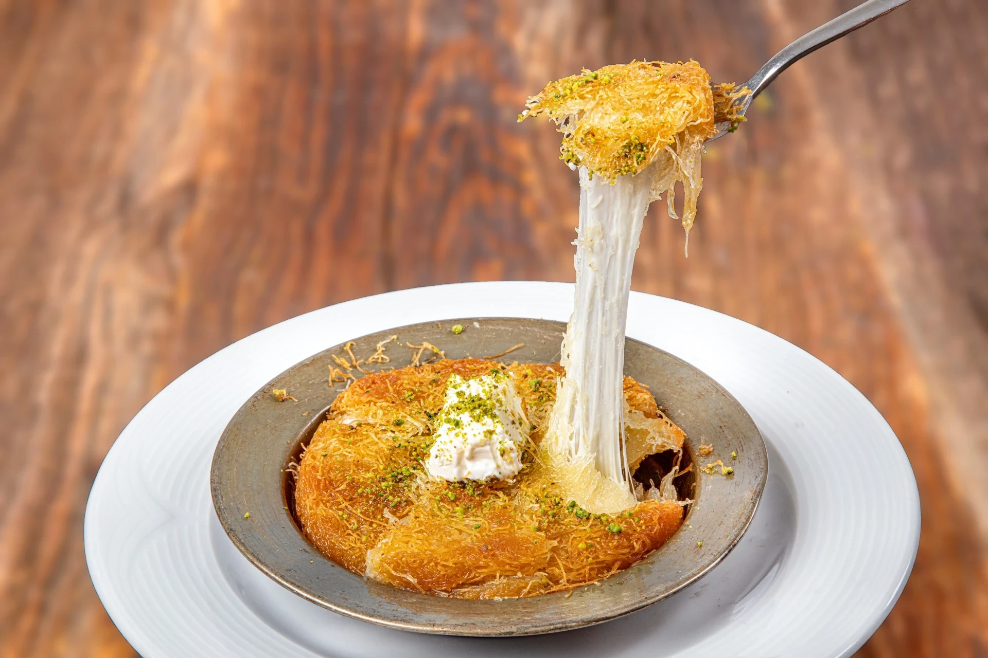 Knafeh, a traditional Middle Eastern dessert, featuring layers of crispy pastry and sweet cheese, drizzled with syrup.