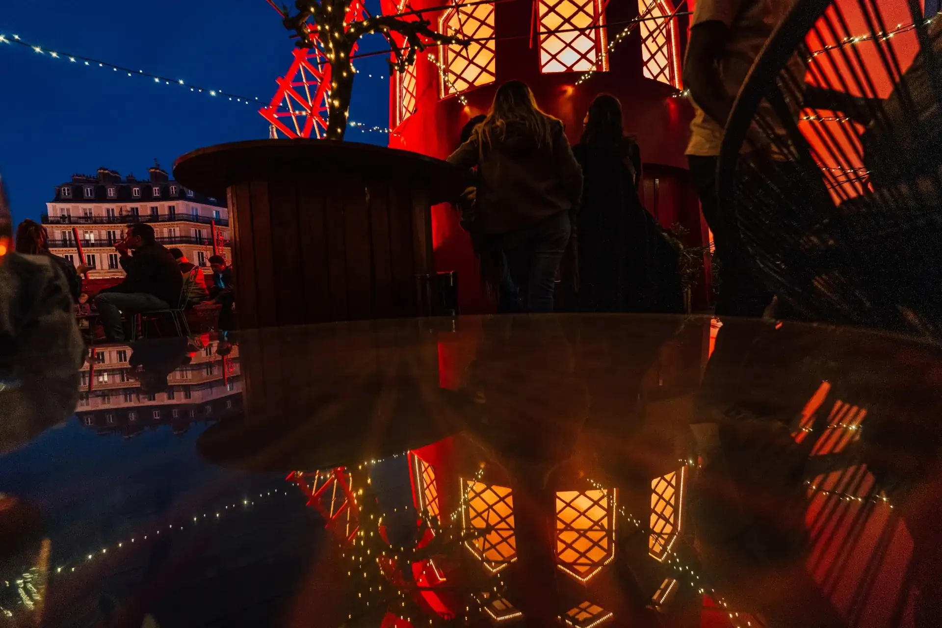 The Moulin Rouge illuminated at night during a French sunset. The iconic red windmill spins, casting vibrant red lights in the evening sky.