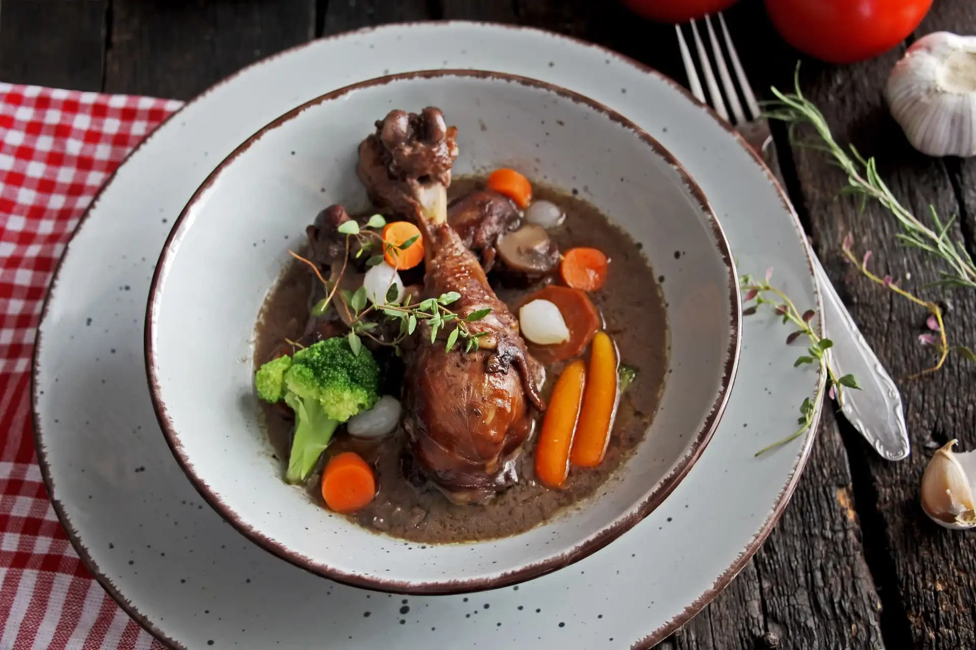 Coq au Vin served on a plate on a wooden table, accompanied by a red gingham napkin.