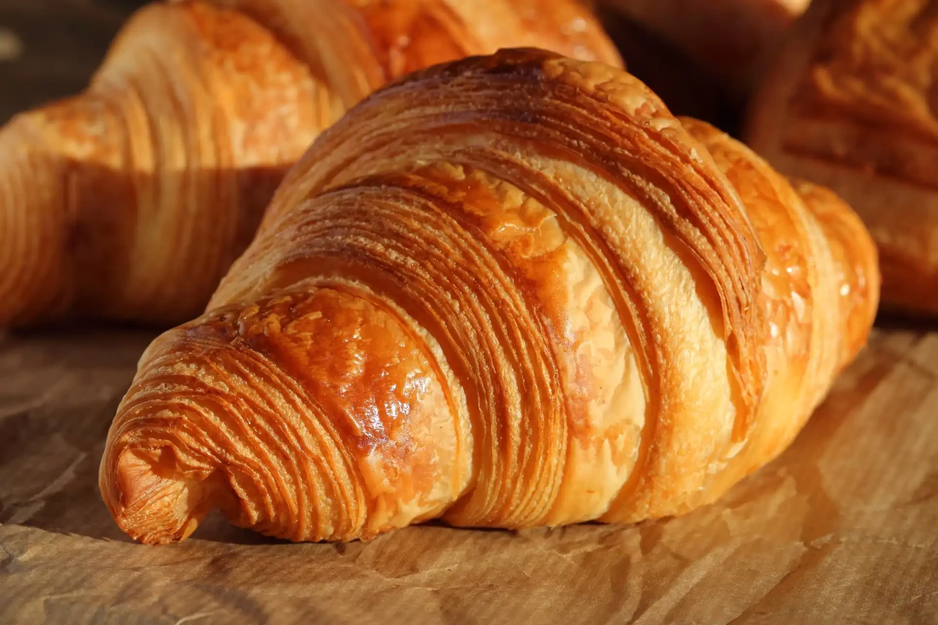 A close-up of a flaky, buttery croissant resting on a brown paper bag.