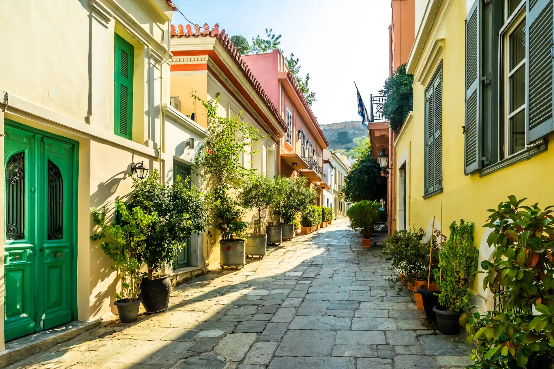 Colourful buildings in the Plaka district of Athens, Greece, near the Acropolis. A cobblestone pathway with potted plants lining the street.