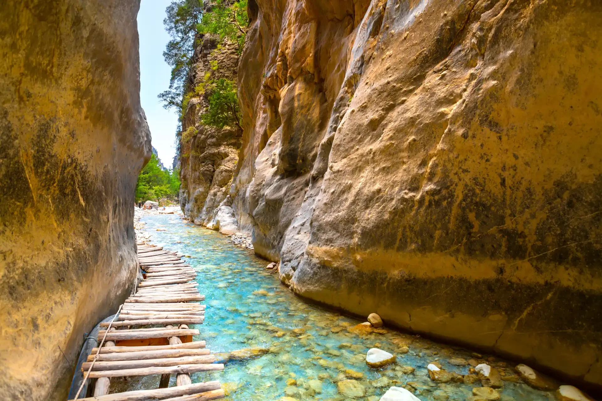 Hiking trail in Samaria Gorge National Park on Crete, Greece. Turquoise waters flow between towering rocks with a pathway made of wooden sticks.