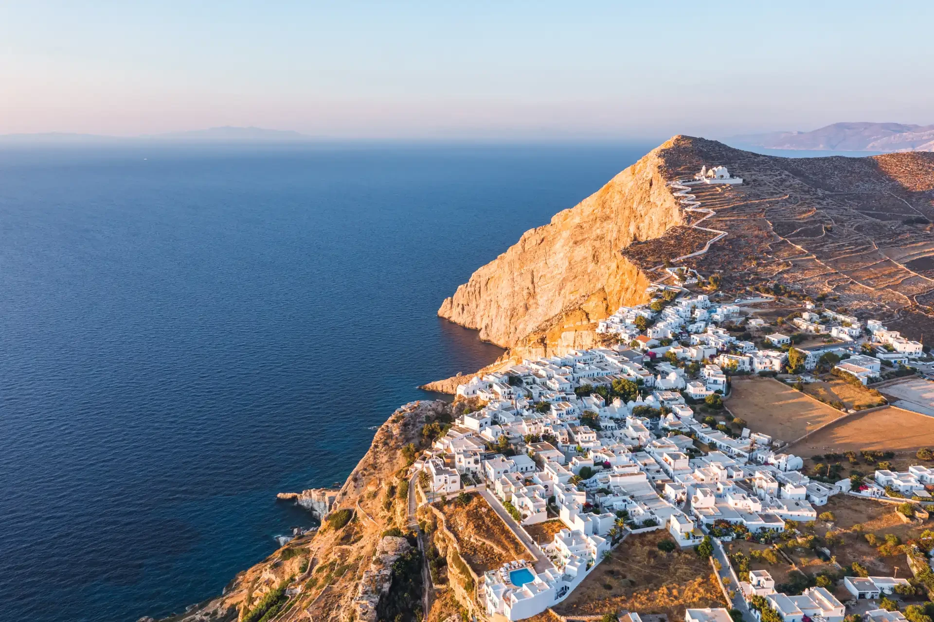 Aerial view of Folegandros Island in the Cyclades, Greece. Blue sea surrounds white buildings perched on cliff edges.