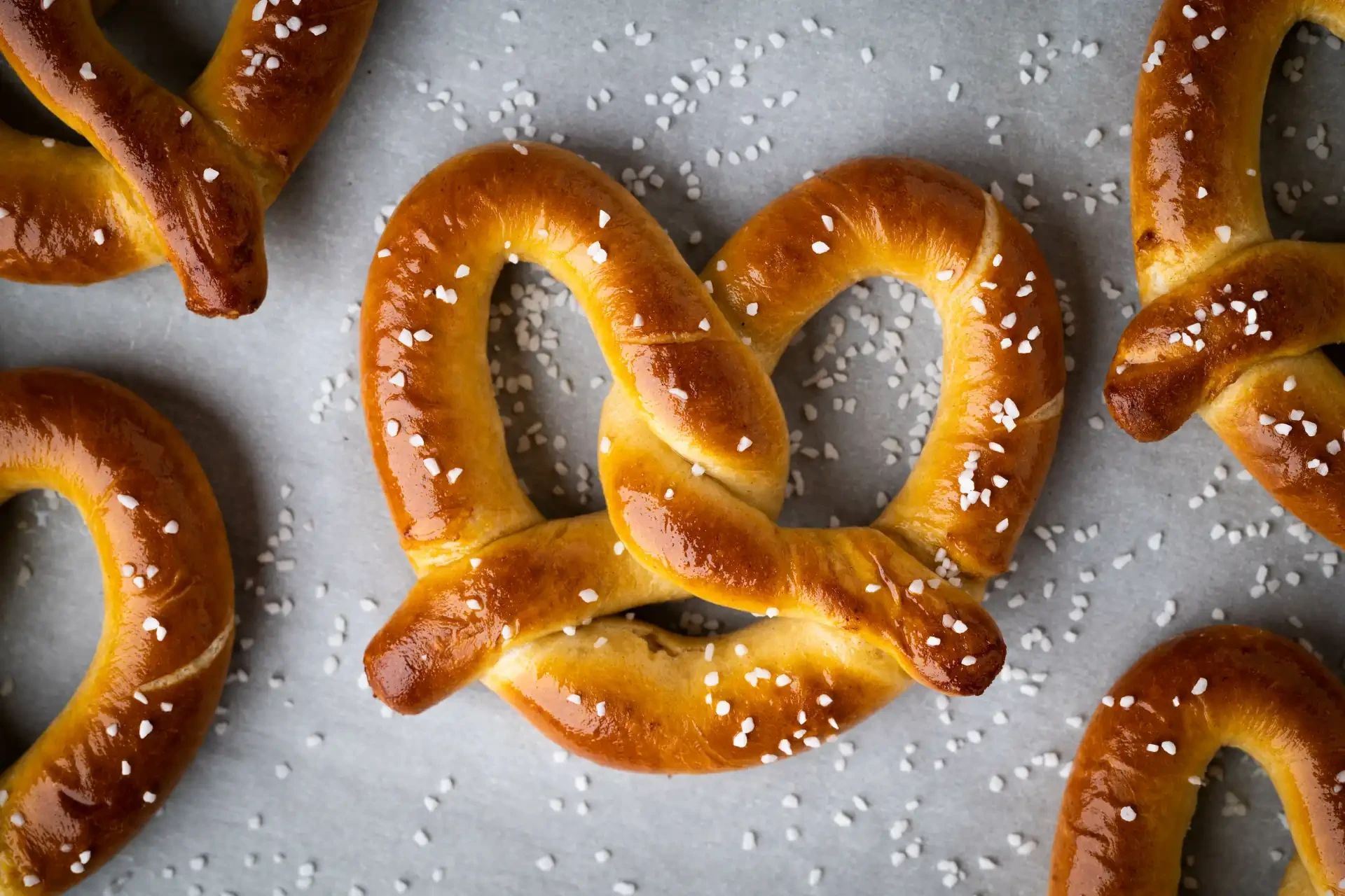A freshly baked pretzel on a cooking pan, showcasing its twisted shape and golden-brown crust. Sea salt is sprinkled over the top.
