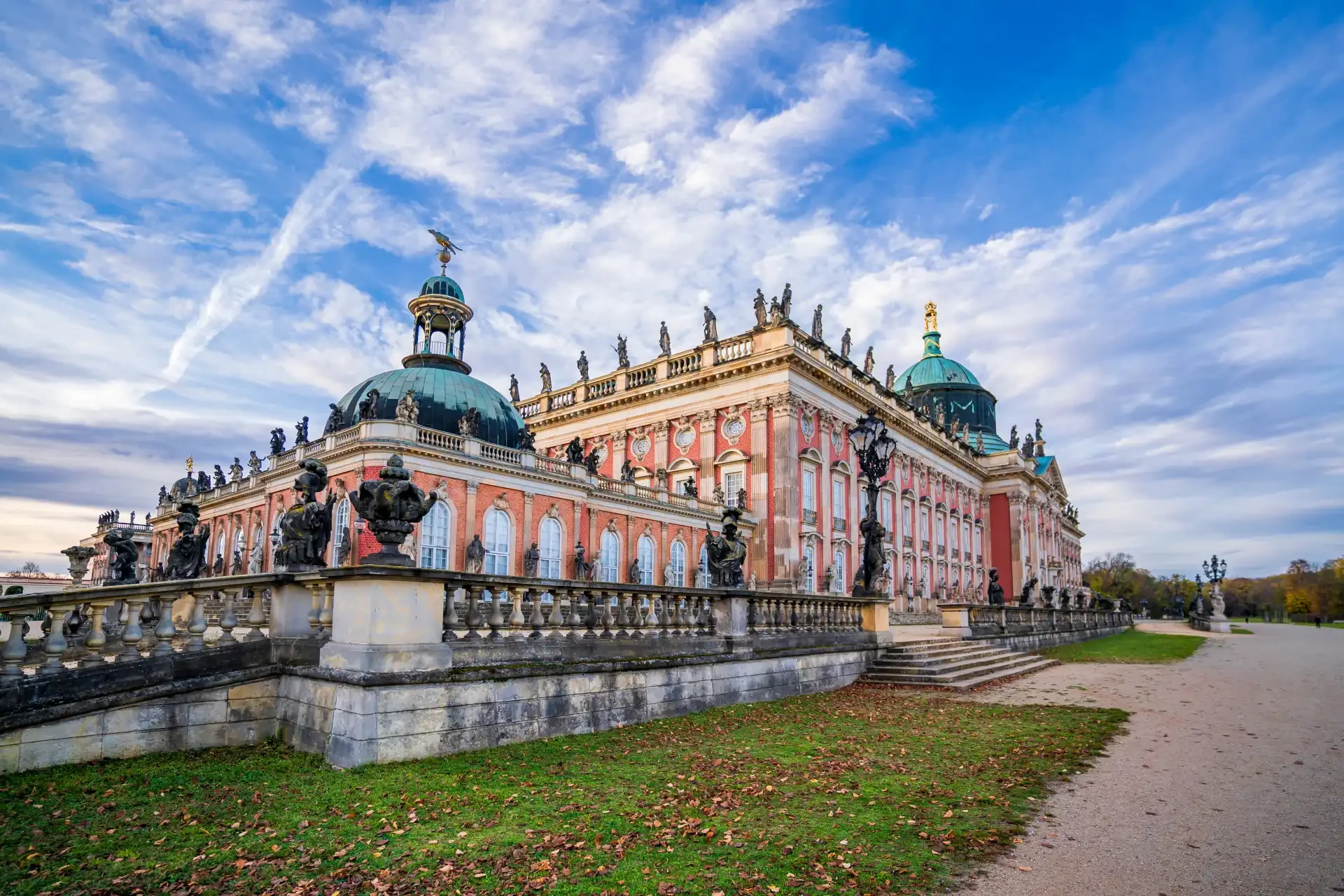 The New Palace buildings in Potsdam, Germany, part of the Sanssouci Palace complex, displaying grand Baroque architecture. Fallen leaves are scattered on the surrounding lawns.
