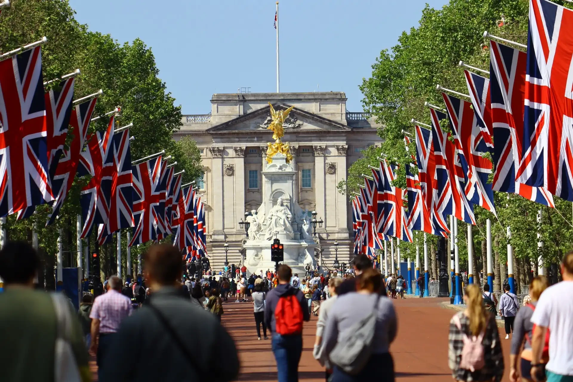 A crowd of people walking along the path to Buckingham Palace, the official residence of the British monarch. The path is lined with flags of Great Britain.