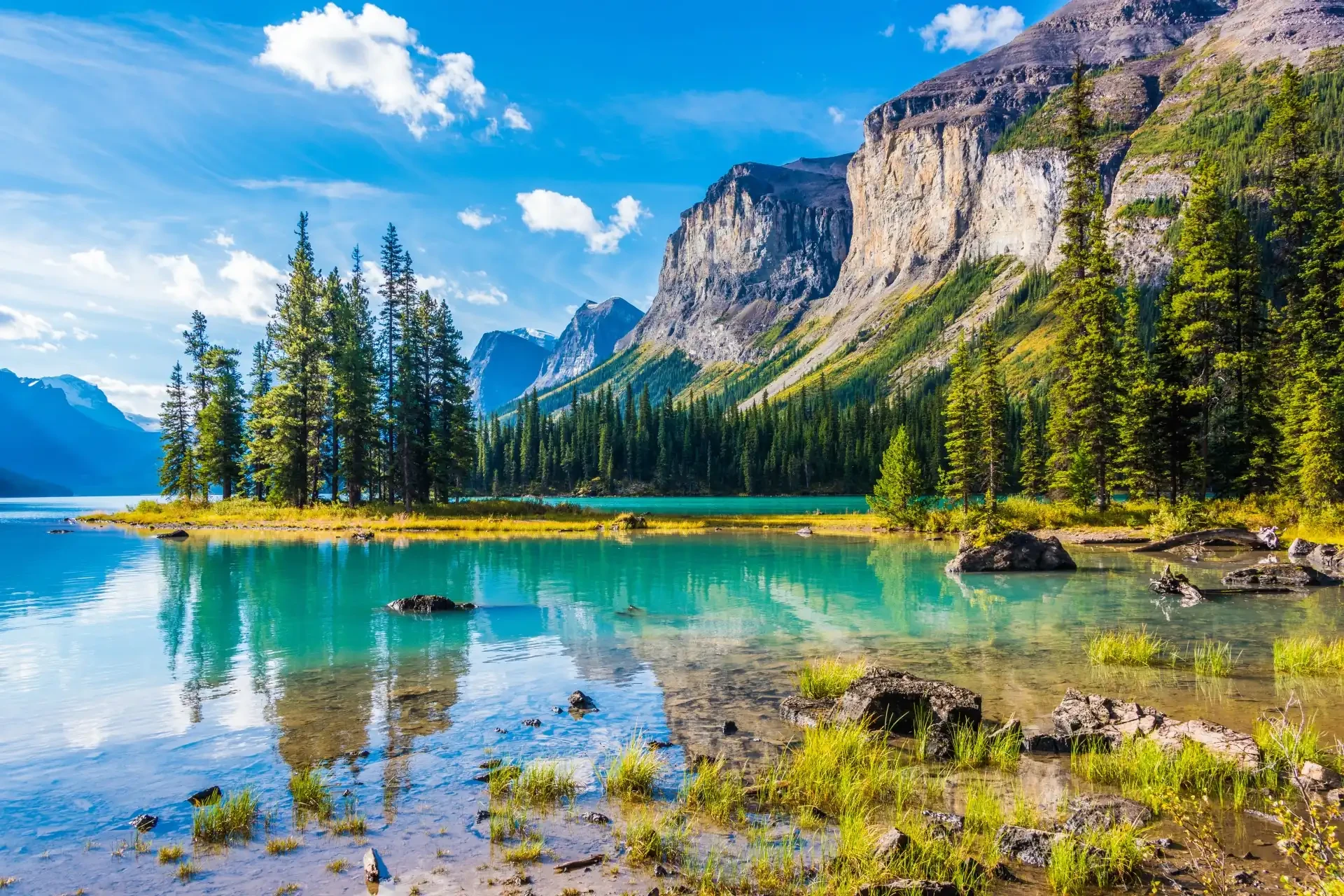 Jasper National Park in Alberta, Canada, featuring a stunning turquoise lake under a blue sky adorned with fluffy clouds.