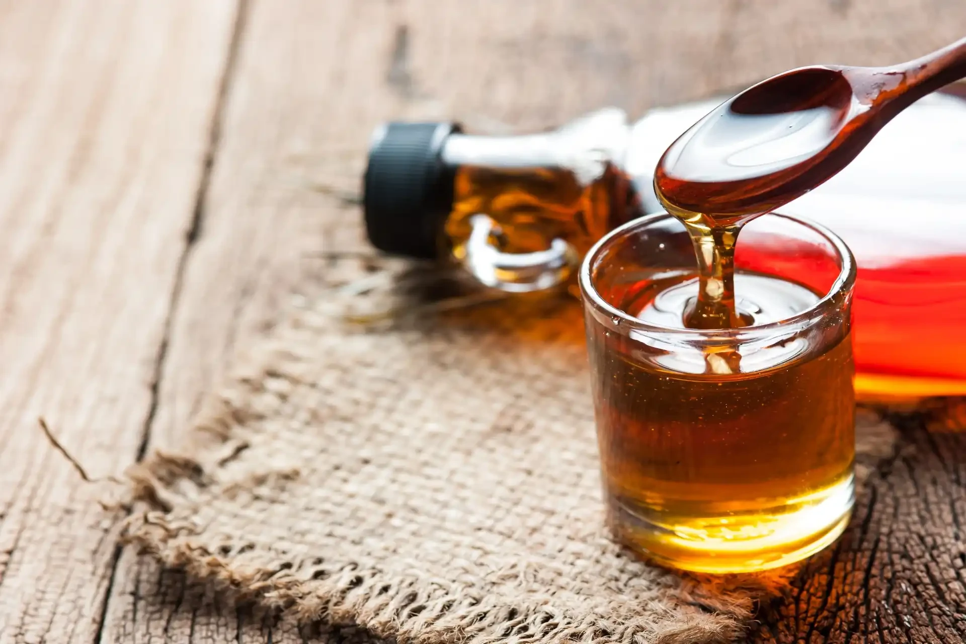 A glass cup filled with rich and amber-coloured maple syrup, a sweet and iconic Canadian product harvested from maple trees.