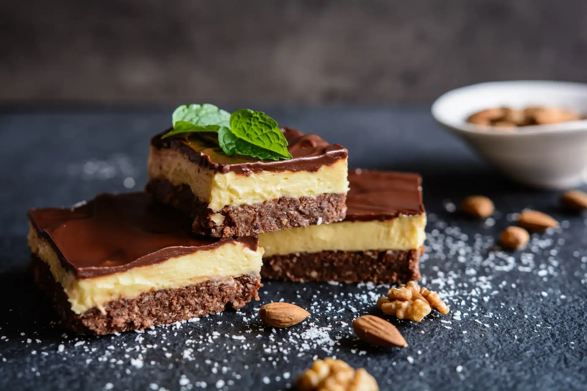 Nanaimo Bars, a classic Canadian dessert consisting of layers of chocolate, custard, and coconut. Pictured on a slate board topped with a mint leaf.