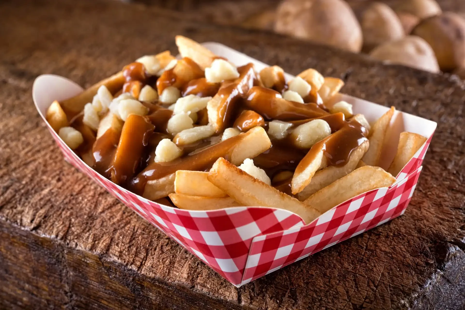A serving of poutine, a classic Canadian dish, featuring fries topped with cheese curds and gravy, presented on a gingham cardboard tray.