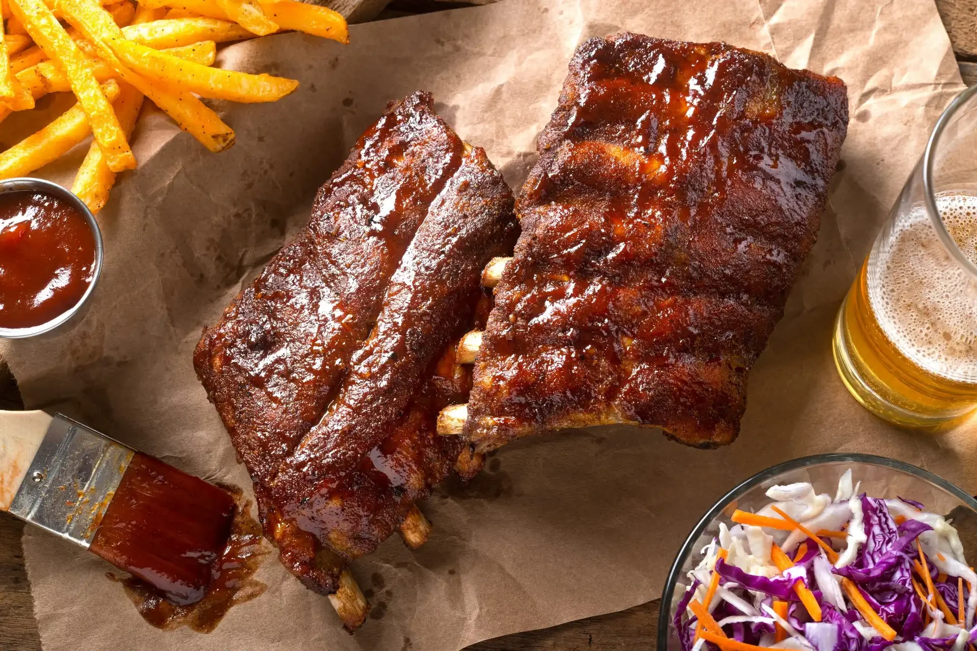 A close-up of succulent barbecue ribs with a glossy glaze, served with a side of fries and coleslaw.