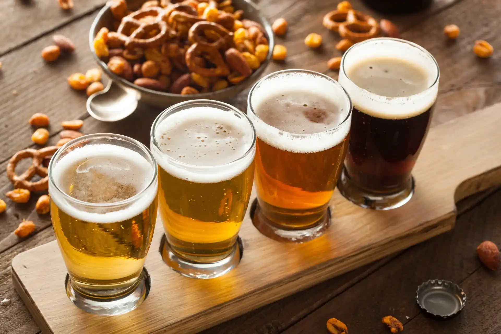 A flight of craft beers on a wooden tasting board, showcasing different colours and styles of beer.