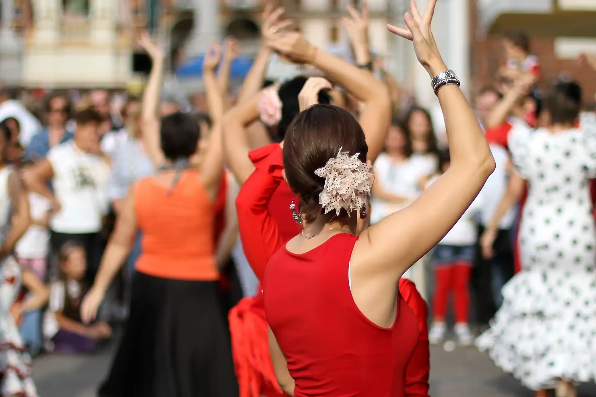 A flamenco dancer wearing a red dress takes centre stage, surrounded by others dancing in the background, capturing the vibrant energy of a flamenco performance.