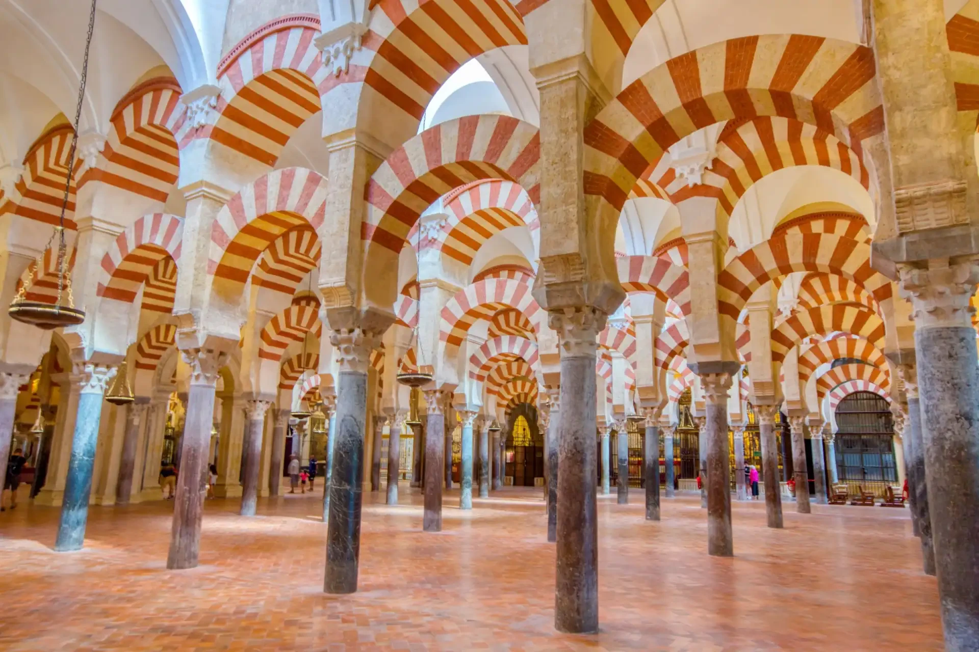 Inside the Mezquita Cathedral in Cordoba, Spain, the intricate vaulted ceiling is highlighted, characterised by orange-striped patterns that add to the architectural beauty of the space.