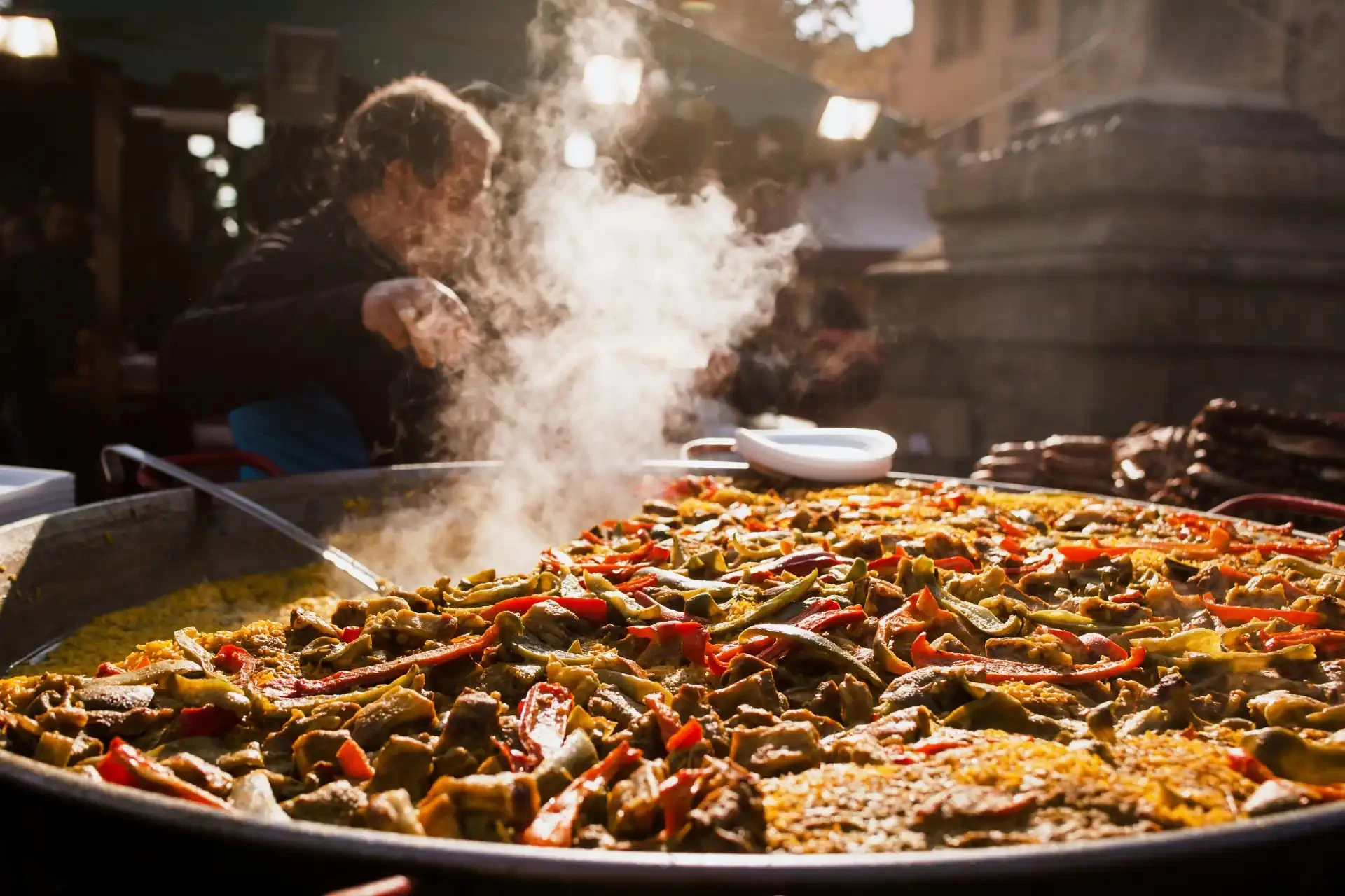 A man is seen cooking paella, a traditional Spanish dish, in Valencia. The dish, typically cooked in a large pan, is a colourful mix of rice, seafood, meats, and vegetables, simmering over an open flame.
