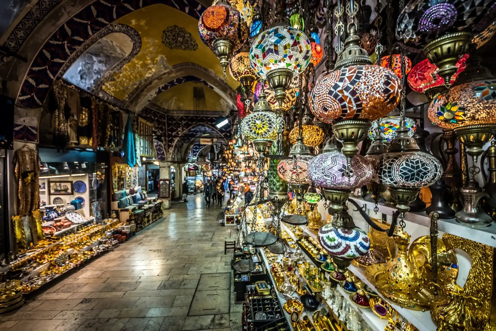 The Grand Bazaar in Istanbul, Turkey, with vibrant colours and various shops offering a wide array of goods. Turkish mosaic lamps can be seen in the foreground.