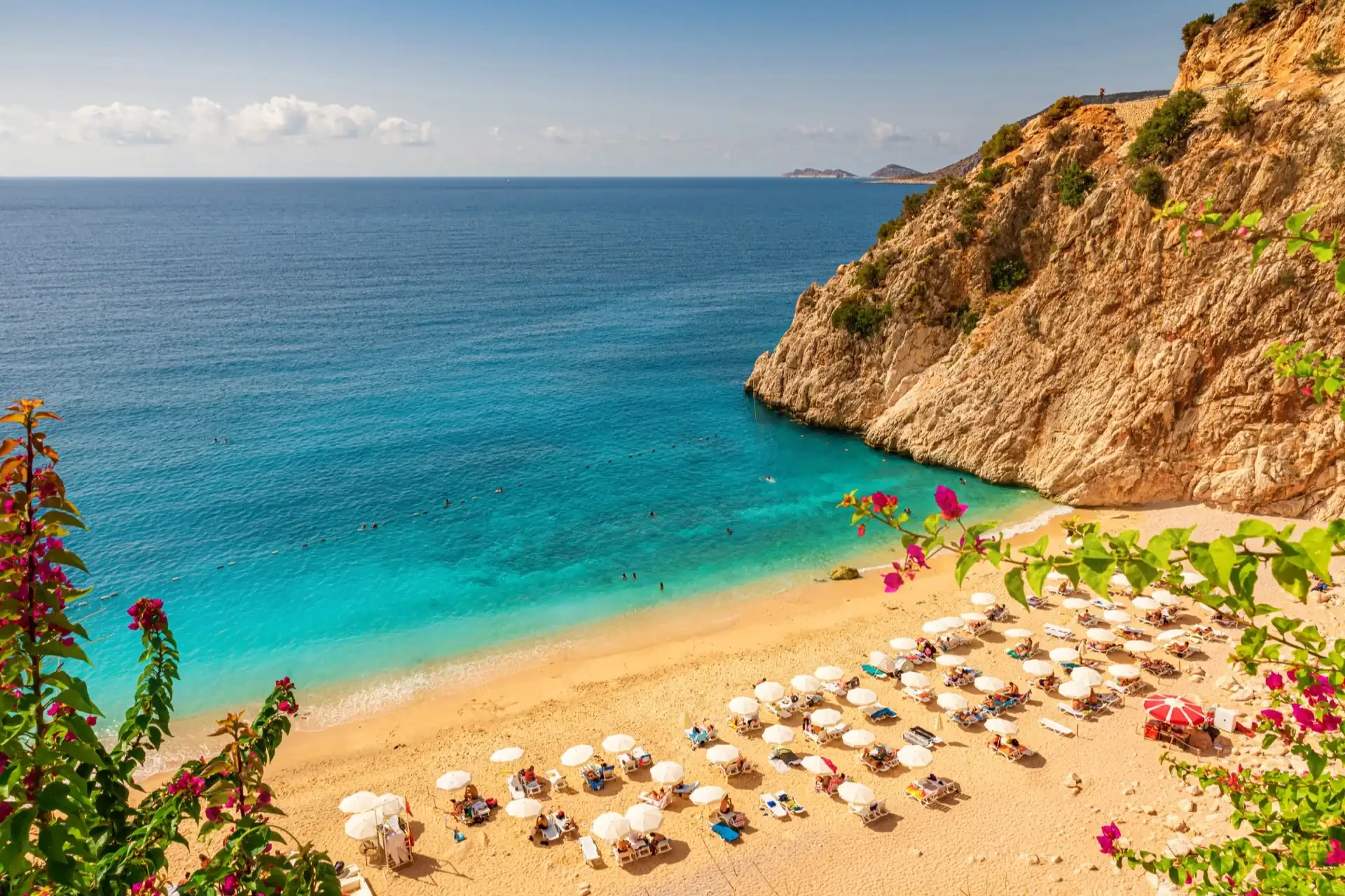 A sandy beach lined with deckchairs and umbrellas faces the turquoise waters of the Antalya coast.